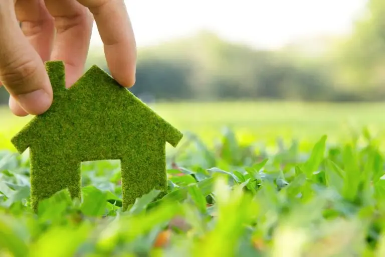 Casa Green. Una mano tiene una casa verde in un tappeto di erba verde
