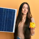 ragazza che tiene in una mano un pannello fotovoltaico e nell'altra un salvadanaio dimostra i benefici del fotovoltaico attraverso le agevolazioni fiscali