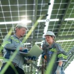 due installatori lavorano sotto le strutture di sostegno dell' impianto fotovoltaico